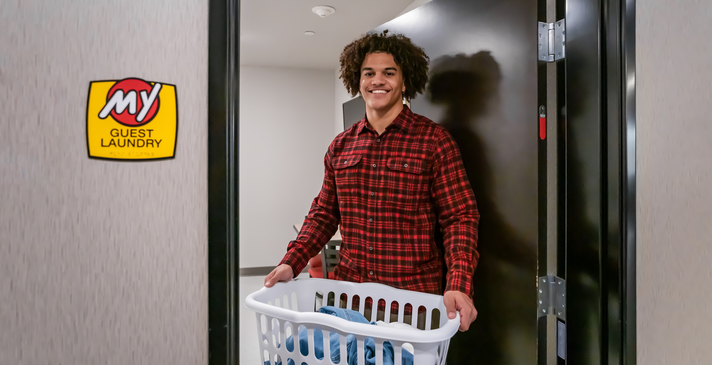 Man leaving the 24 hour on-site laundry facility caring the provided laundry basket full of his clean clothes.