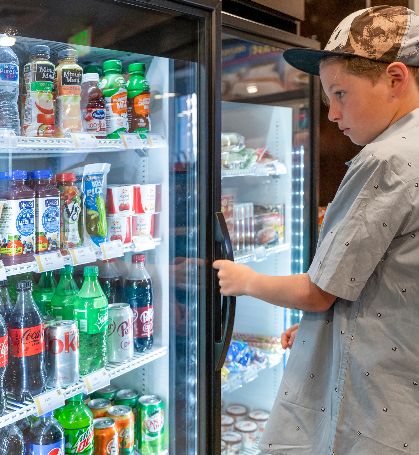 Child wearing a hat deciding what to select out of the drink cooler.