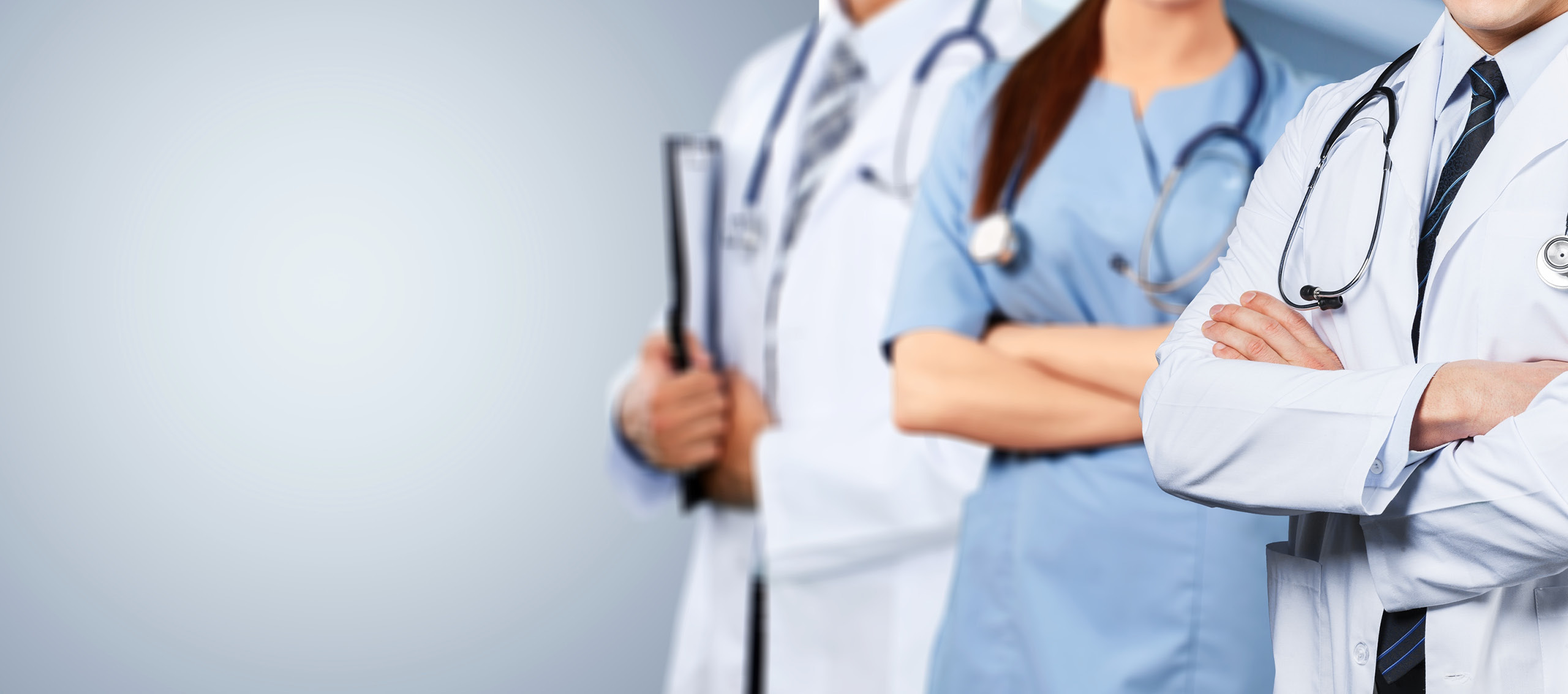 Two doctors wearing lab coats and a nurse wearing blue scrubs all with stethoscopes around their necks and arms crossed.