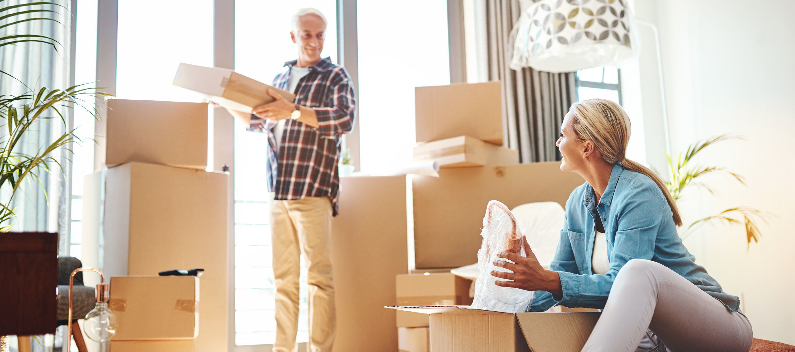 A man and women packing and stacking boxes in front of large glass windows.