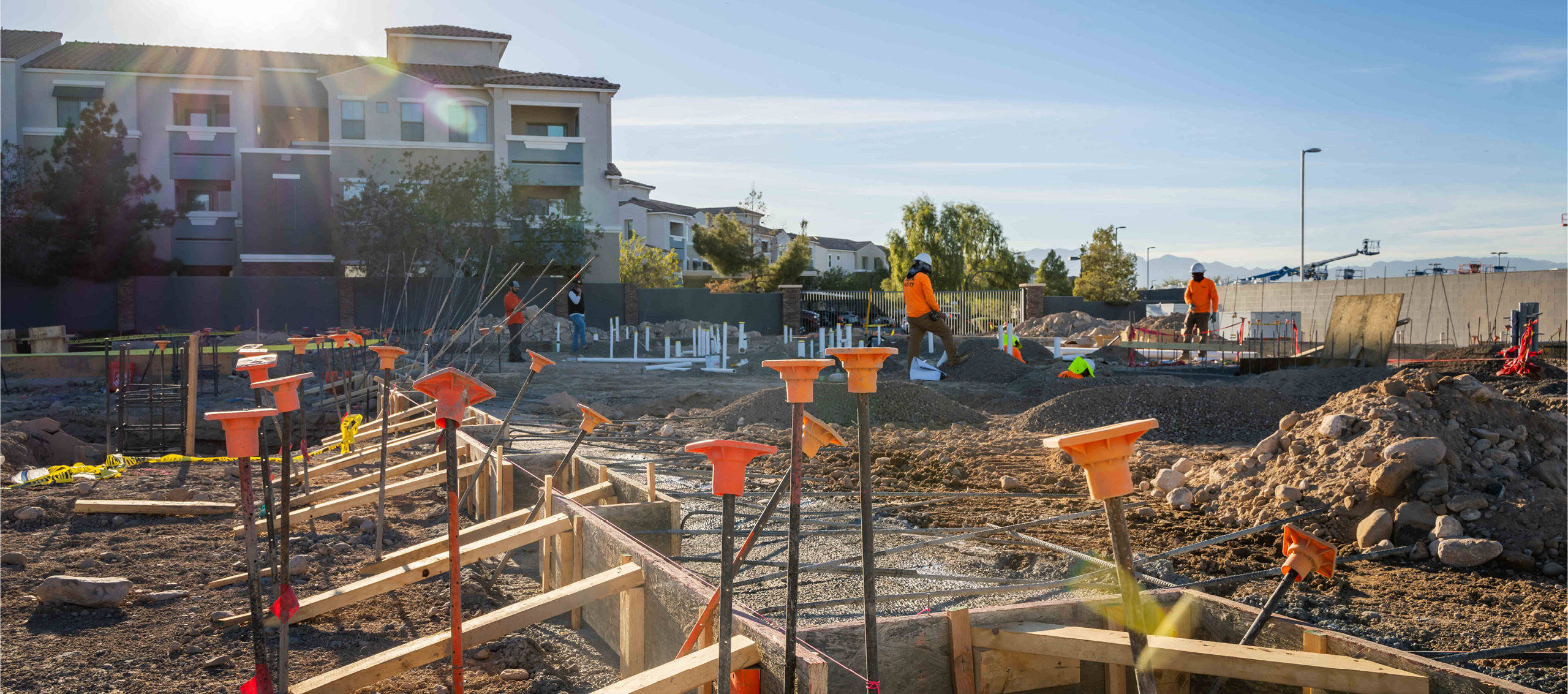 A construction site with concrete framing and metal rods in front of a three story building.