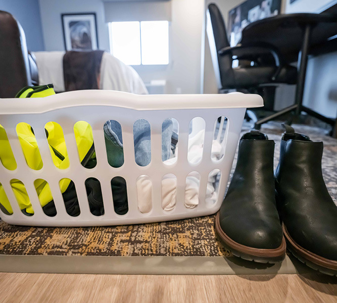 Laundry Basket filled with clothes next to a pair of black boots inside a guest room.