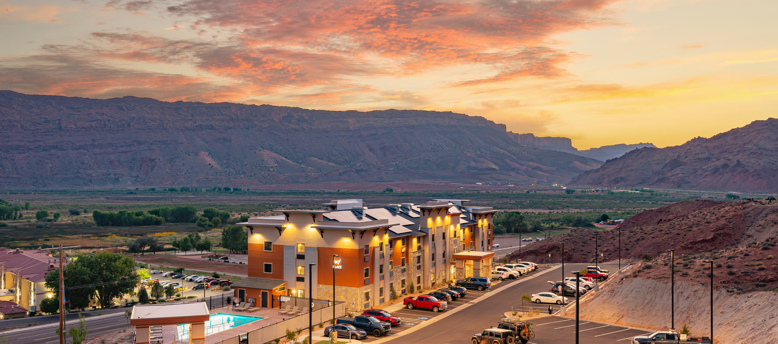 Wide shot of My Place Hotel exterior with mountain landscape and sunset in the background.