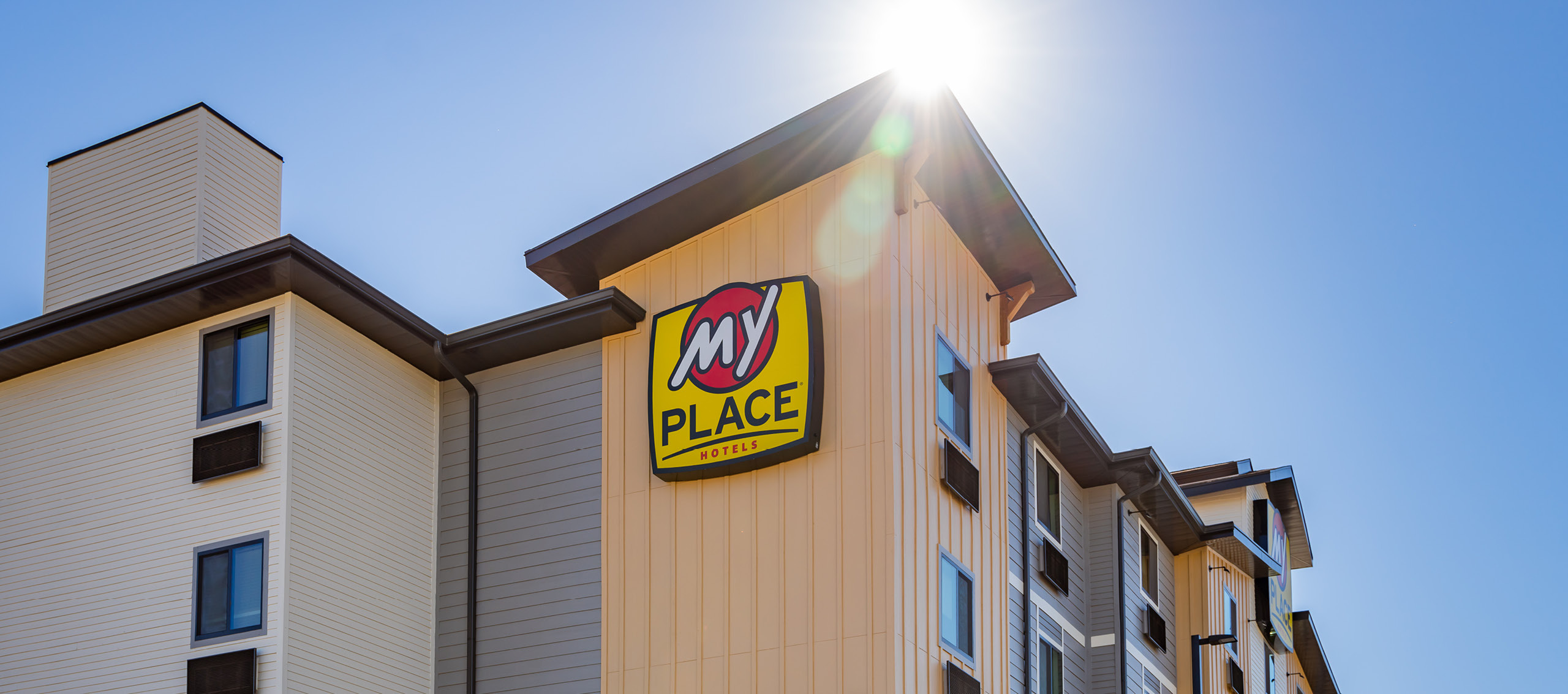 Top half of My Place Hotel exterior with bright sun and clear blue sky.