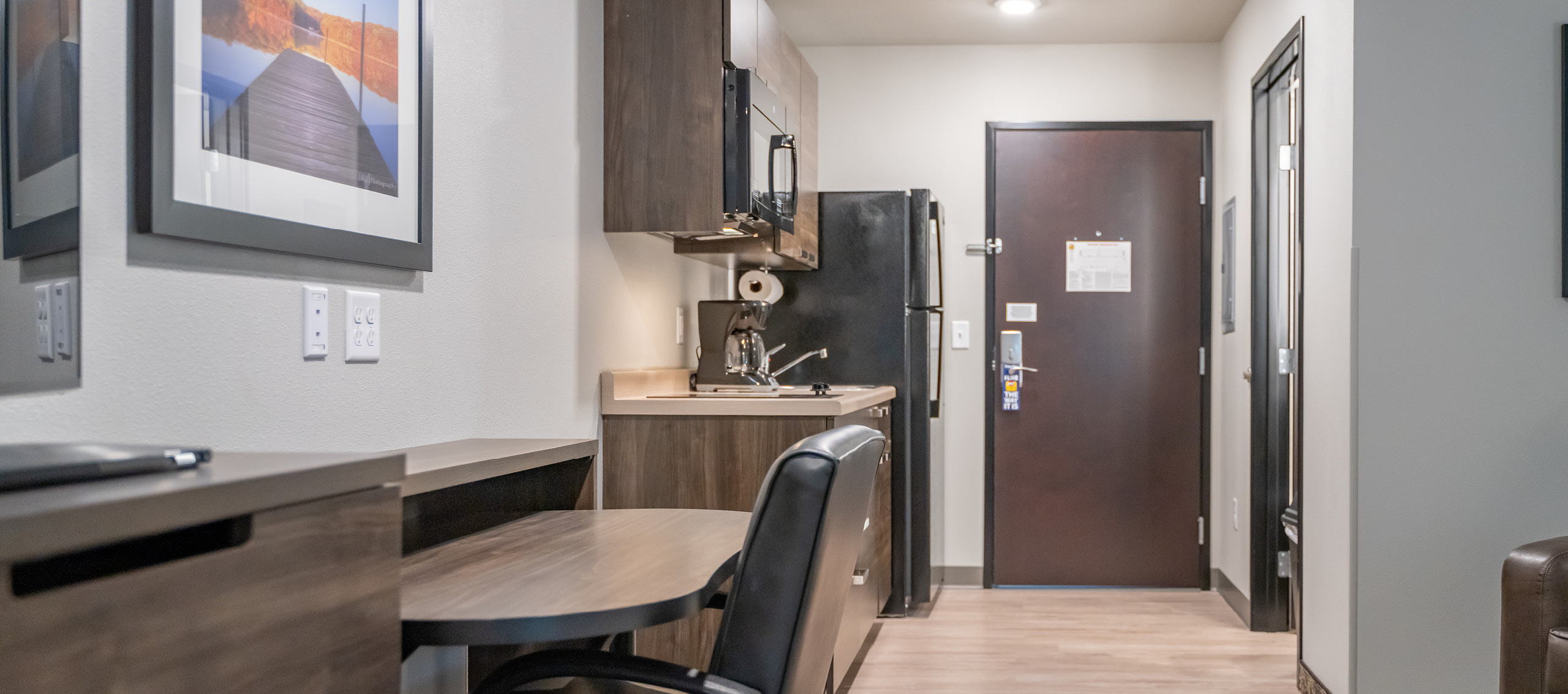 Interior hotel room facing the door with rolling desk, chair, and kitchenette.