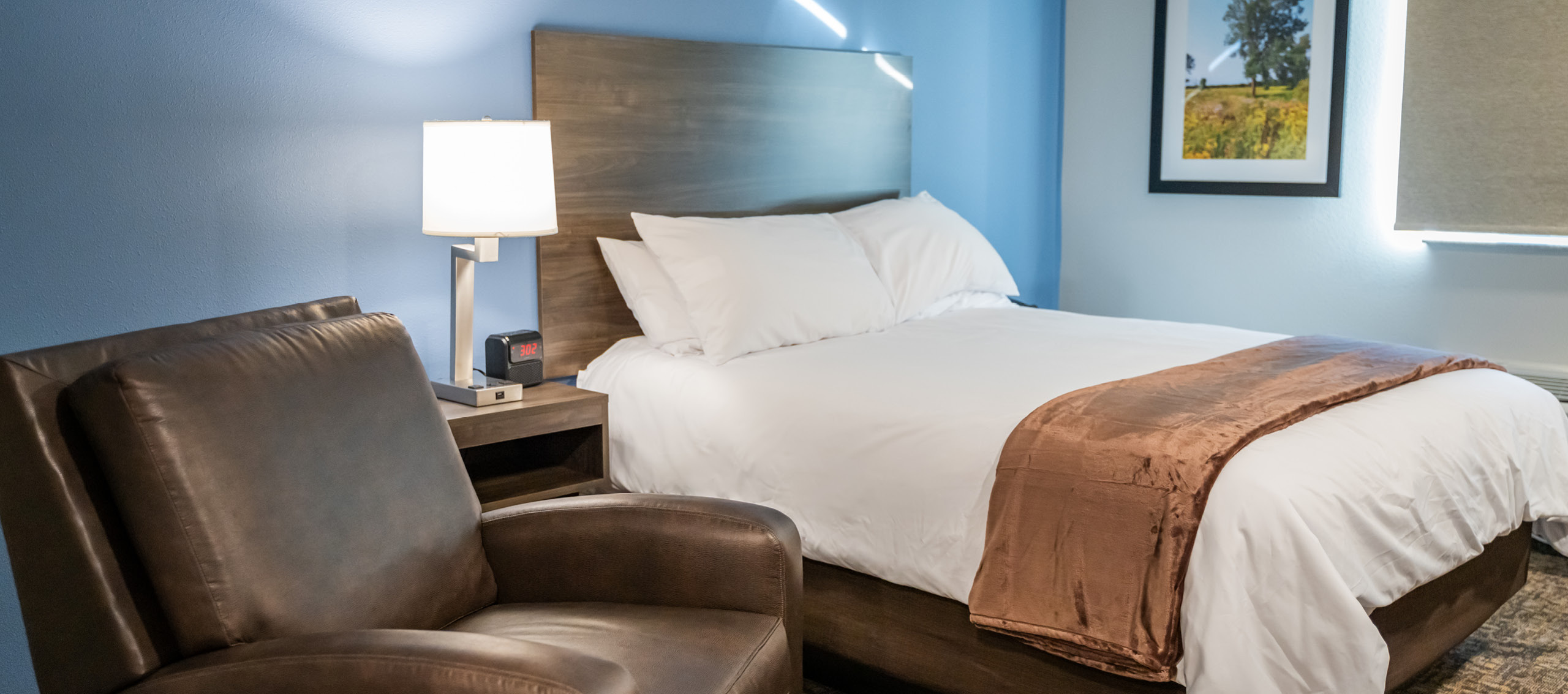 Interior hotel room with single queen bed and brown recliner and a blue accent wall.
