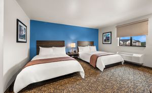 Modern guest room featuring two queen beds, a work desk, flat-screen TV, window, and contemporary furnishings.