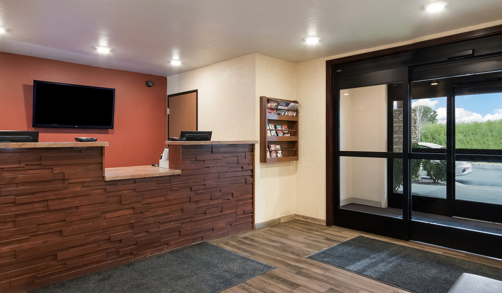 Hotel double automatic doors and front desk with TV and area attraction pamphlets.