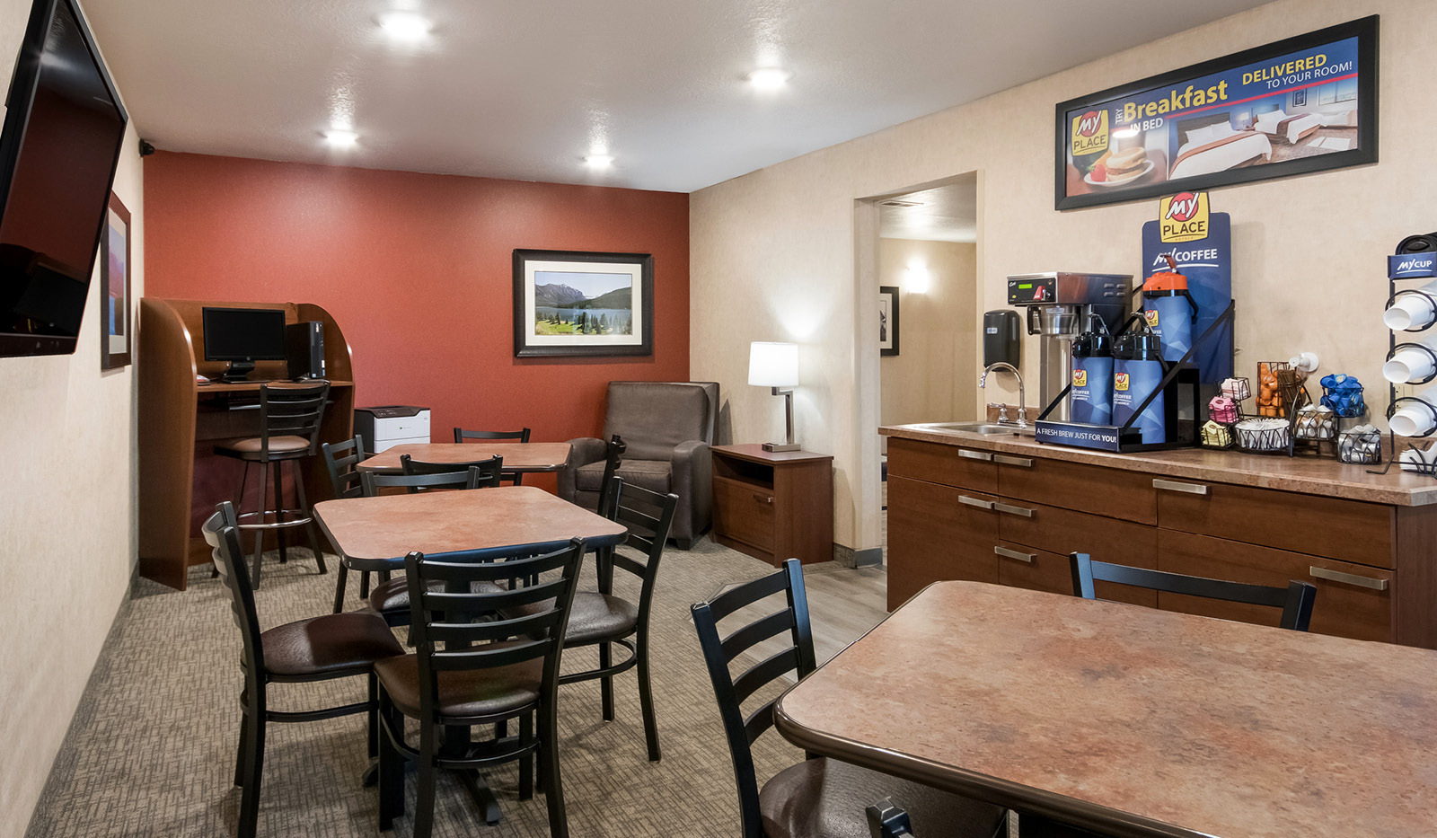 Lobby breakfast area with coffee station, tables and chairs, recliner, and a computer with printer.