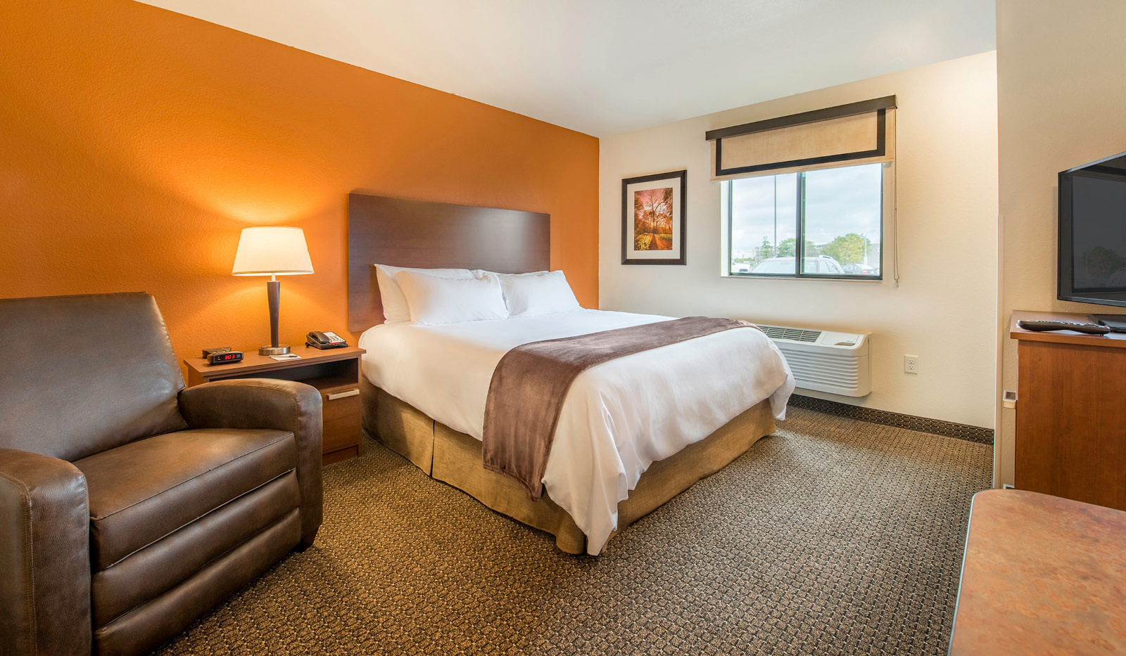 Recliner next to queen bed with side table. In-room climate control under window.