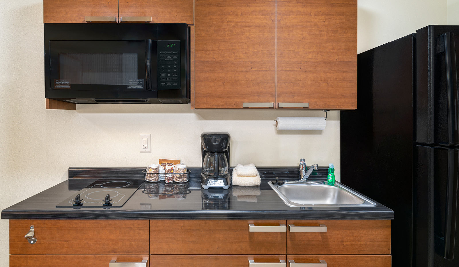 In-room kitchen with two-burner stovetop, coffee maker, sink, microwave, full fridge freezer, paper towels and cupboards.