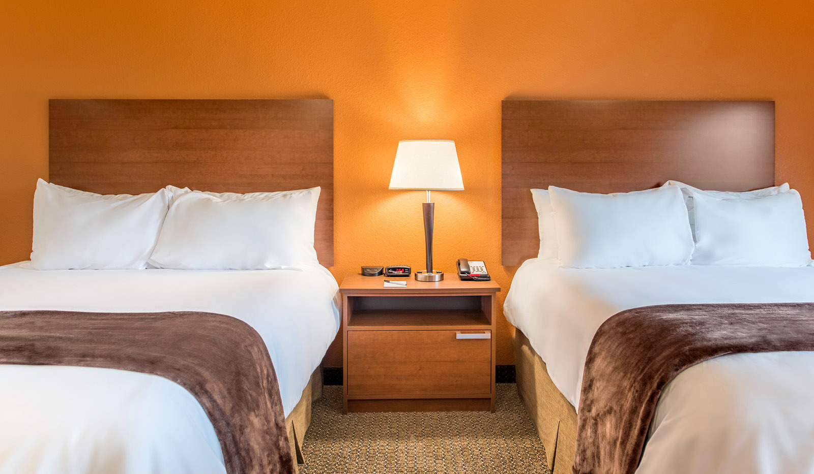 Interior room with bedside table and lamp in the middle, flanked by two queen beds and an orange accent wall.