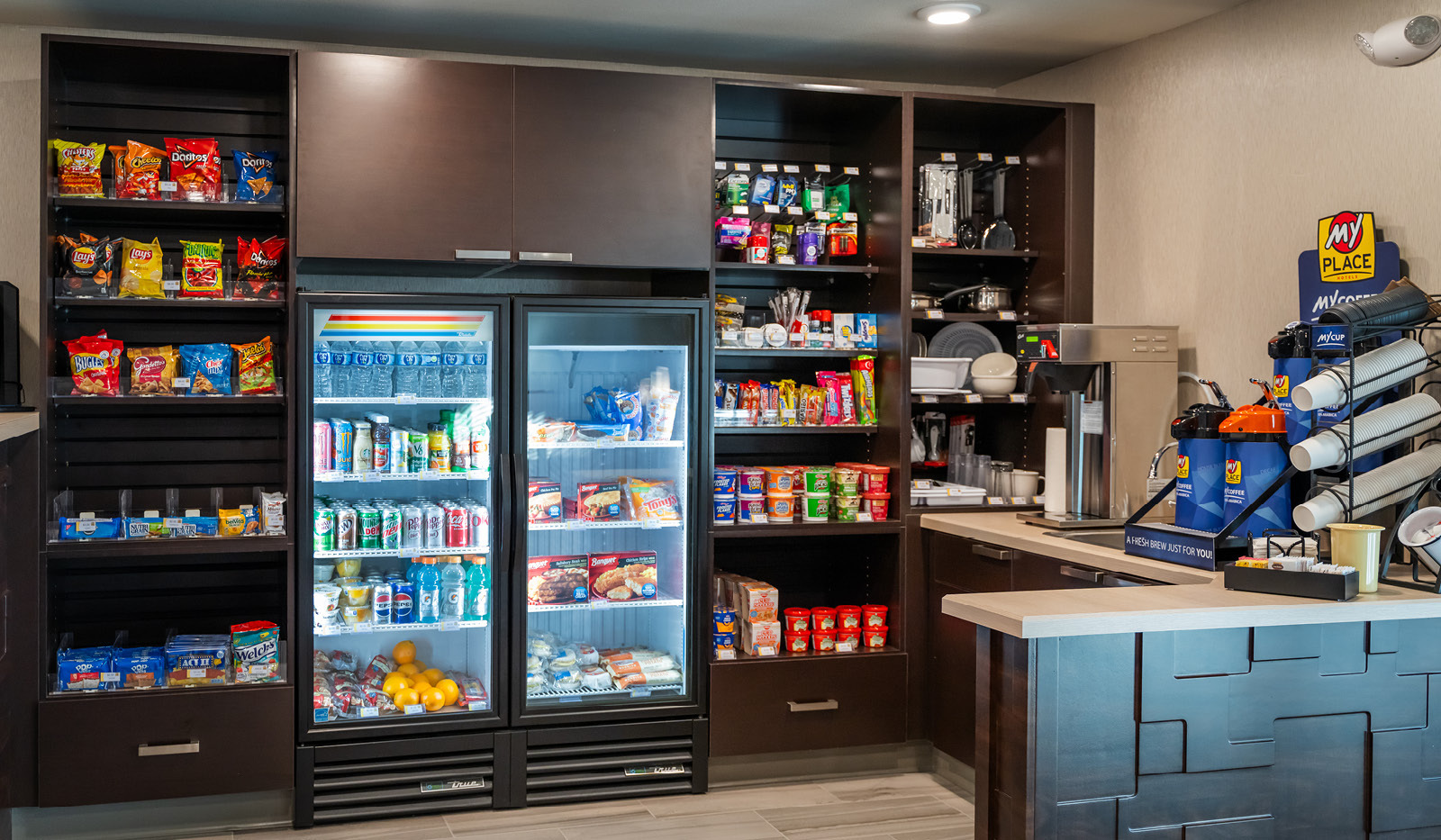Interior lobby's My Store with three rows of snacks and toiletries flanking two coolers of drinks and cold foods, and My Coffee station on the right.