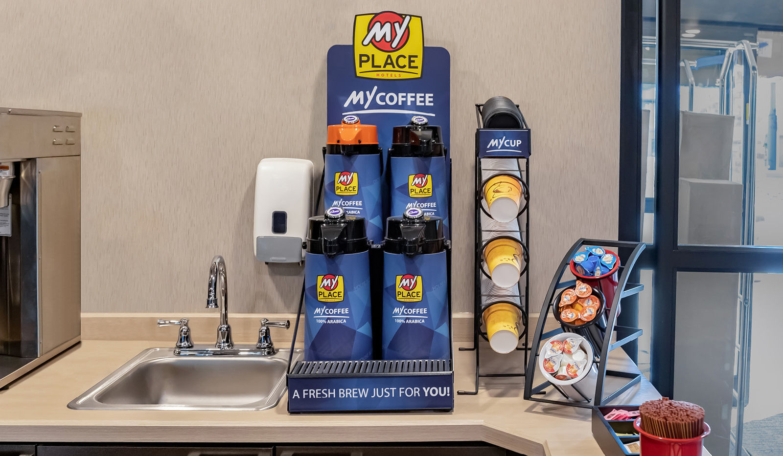 Interior lobby My Coffee station with sink, four coffee carafes, cups, cream and sugar.