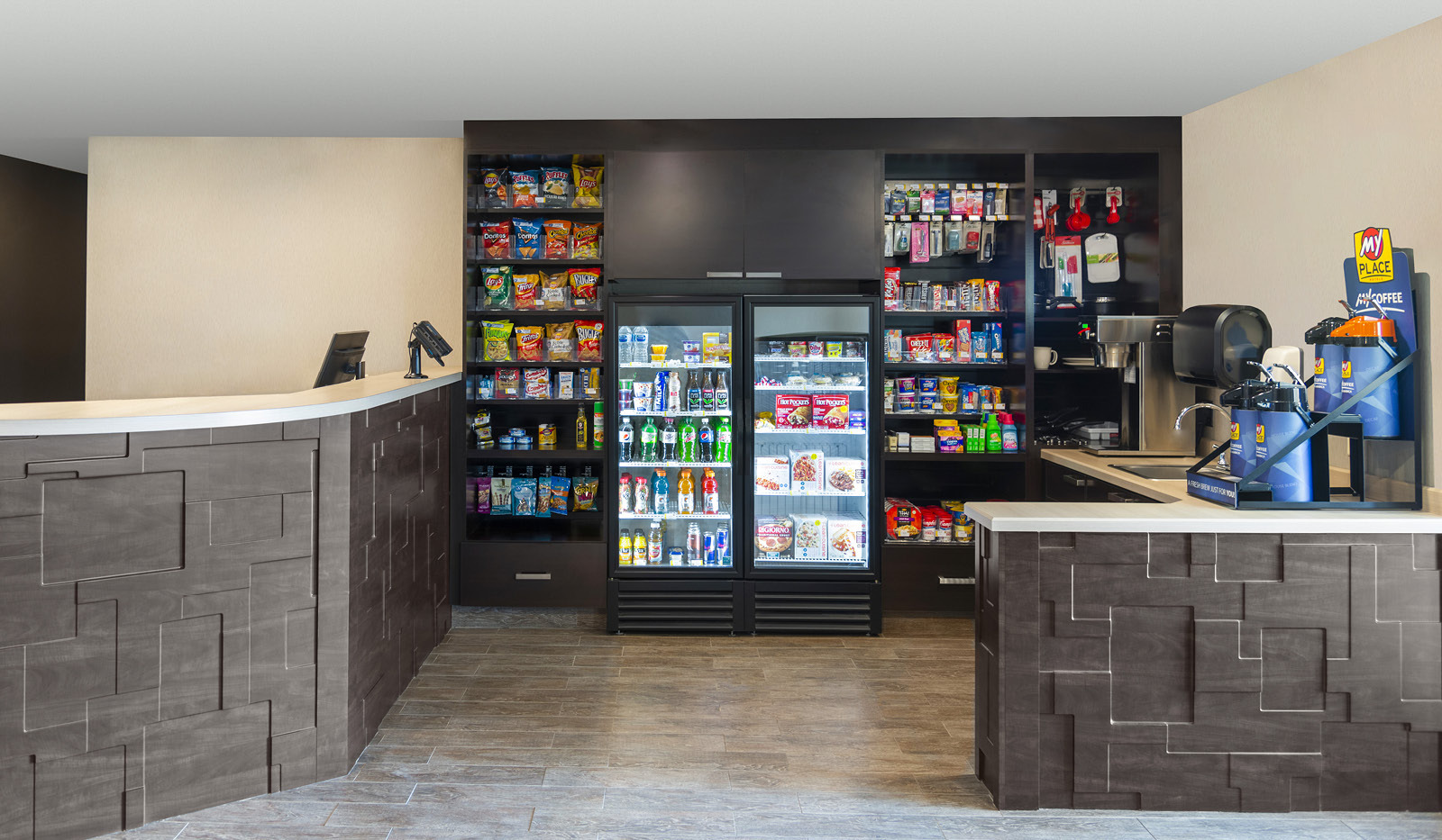 Interior lobby's My Store, with two rows of snacks and toiletries flanking two center coolers of drinks and cold foods, with My Coffee on the right and brown front desk on the left.