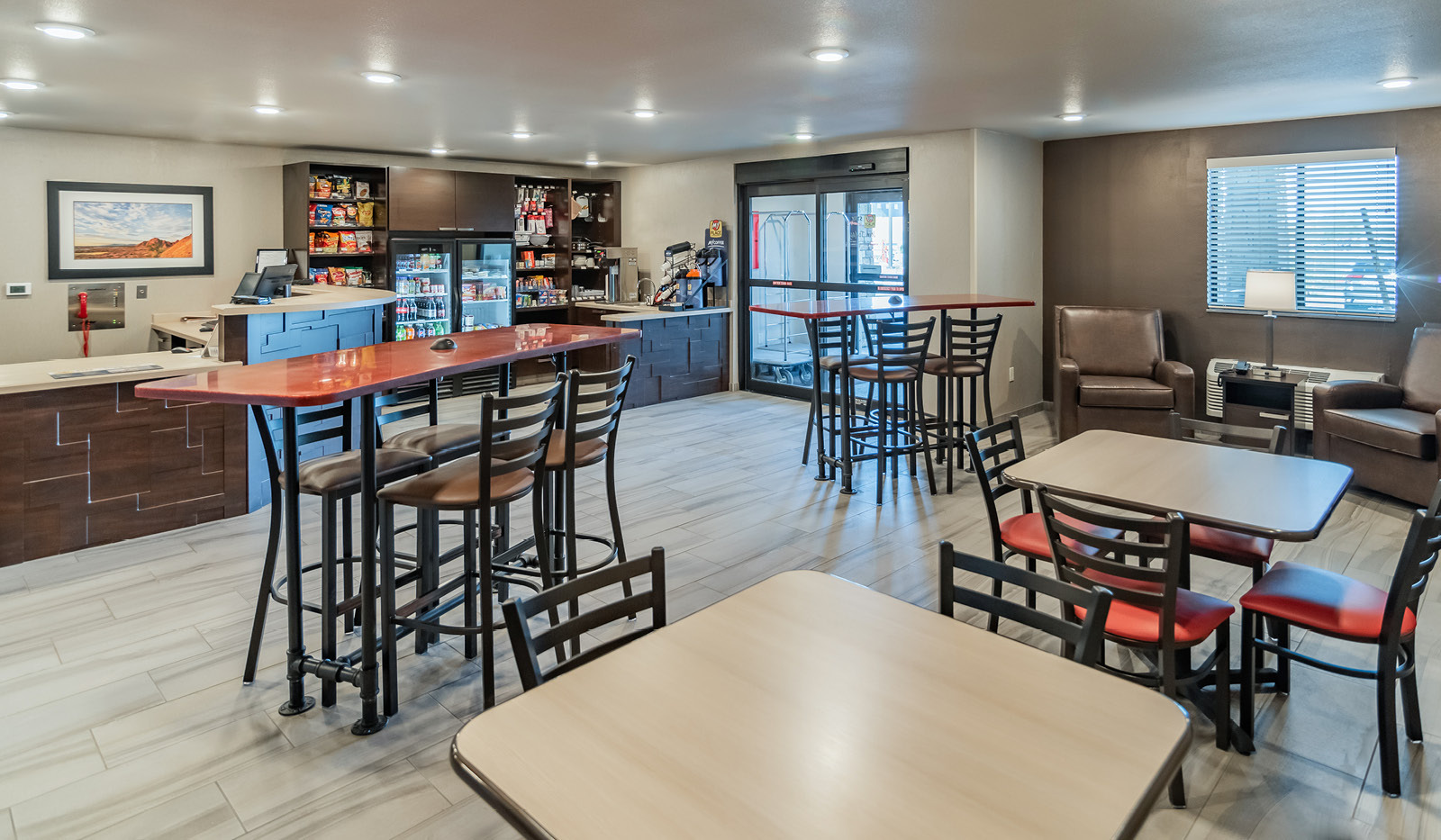 Interior lobby with two counter-height tables and chairs, two bar-height tables and chairs, two brown recliners, and brown front desk and My Store in the background.