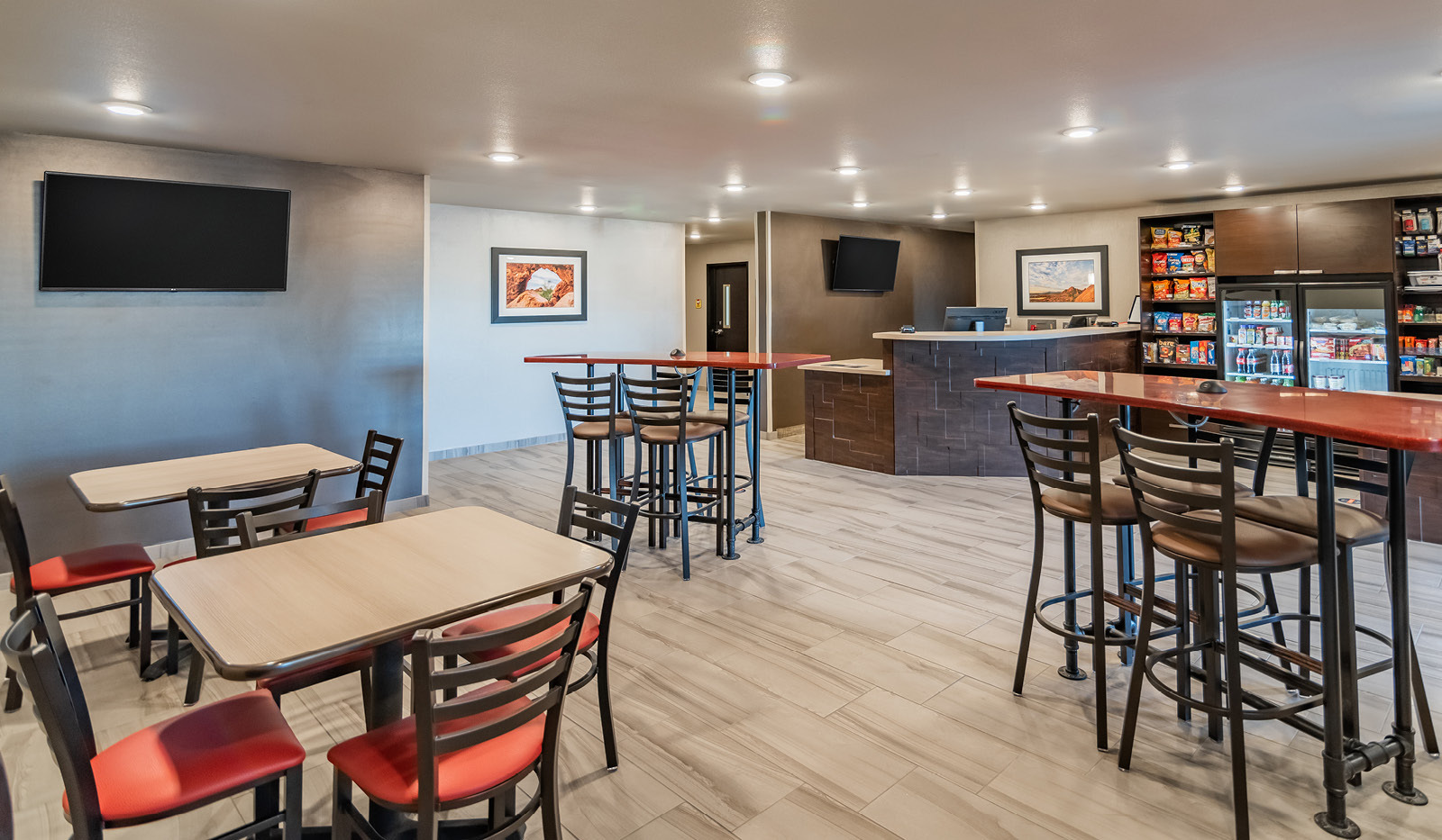 Interior lobby with two counter-height table and chairs, two bar-height tables and chairs, and television, with broth front desk and My Store in the background.