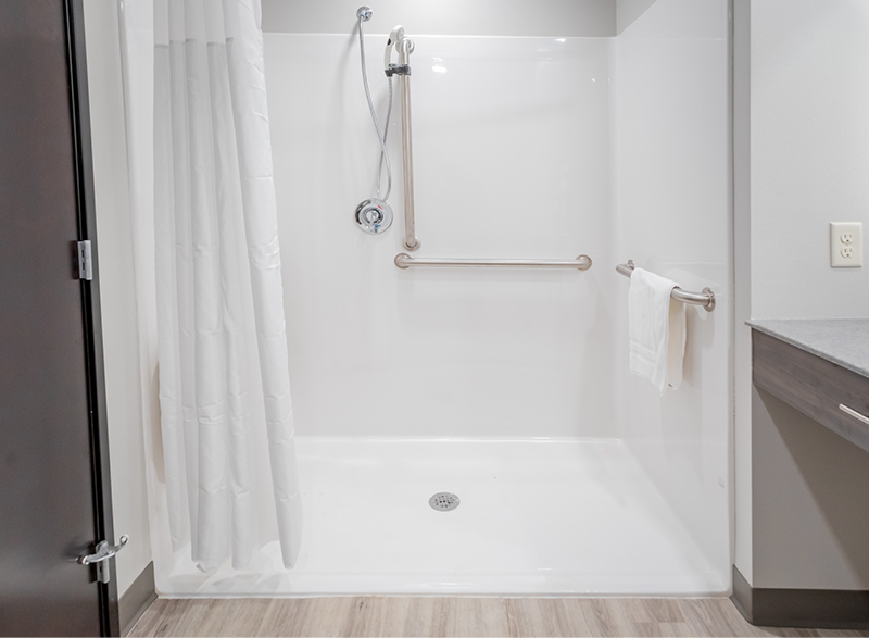 Interior bathroom with white, wheelchair-accessible shower and metal assist hand bars.
