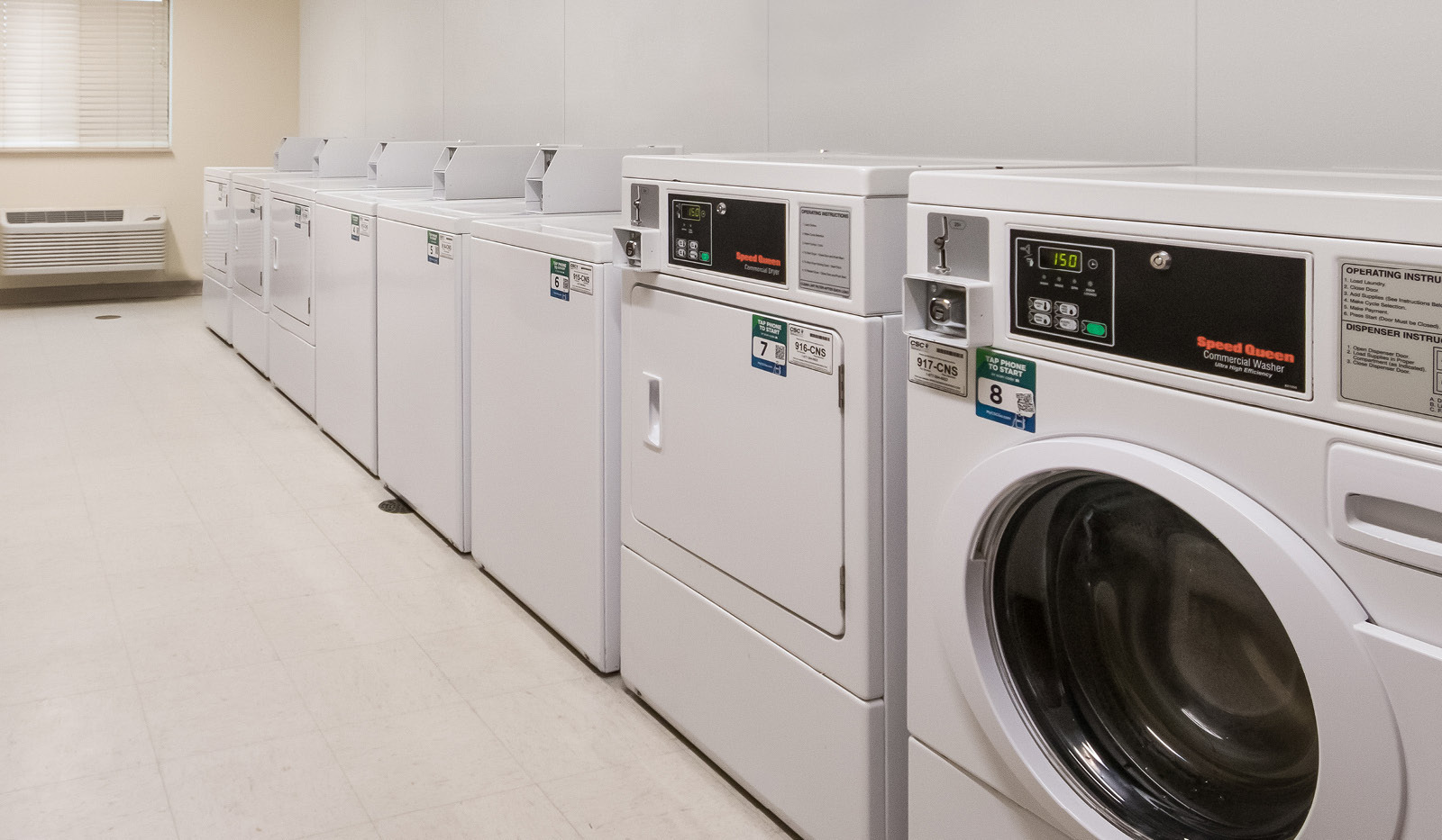 Interior laundry facility with eight coin-operated washer and dryer units.