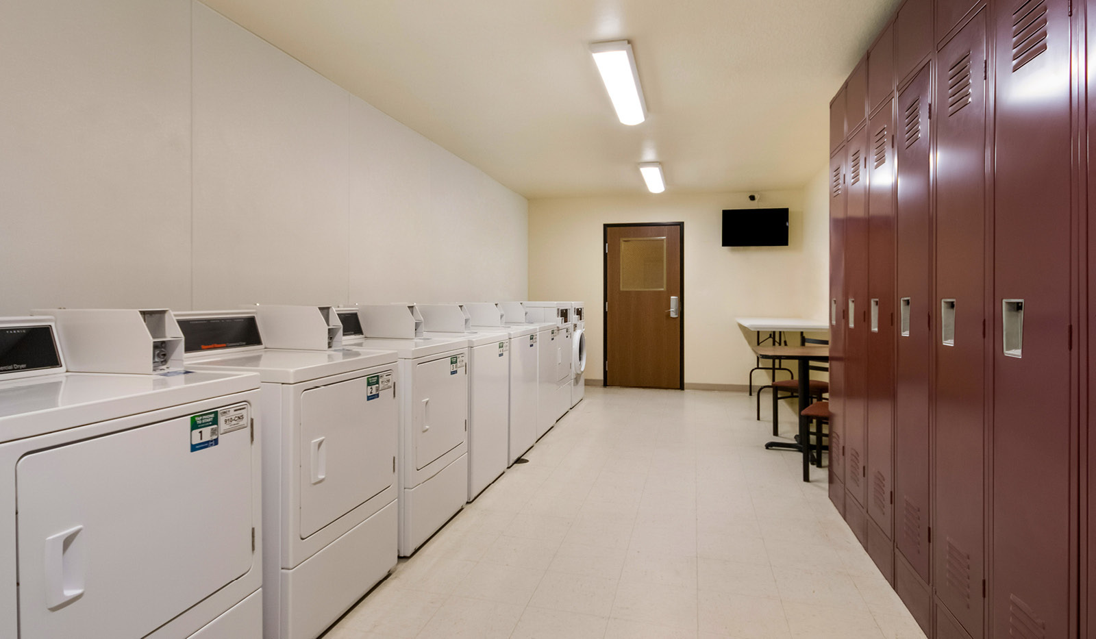 Interior laundry facility with washer and dryer units on the left, and lockers and a table and chairs on the right.