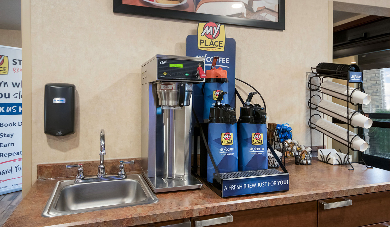 Interior lobby My Coffee station with sink, four coffee carafes, cups, lids, sugar, and cream.