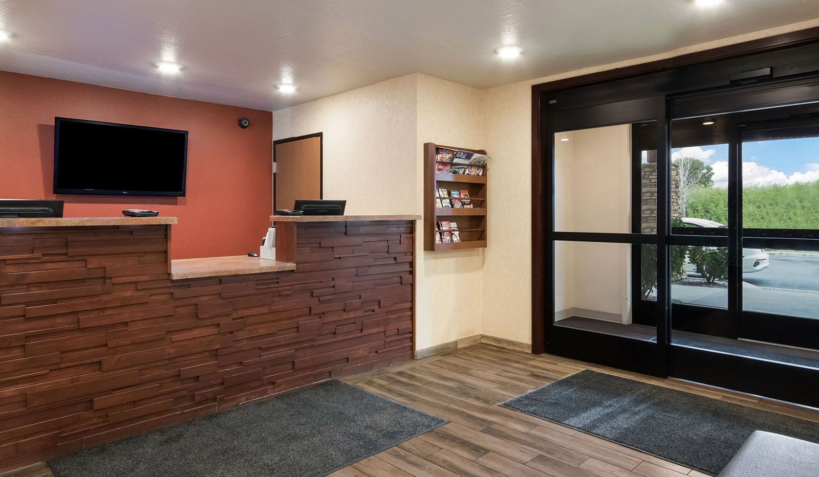 Interior lobby with brown front desk, television behind the desk, door to manager's office, and automatic doors to the right.