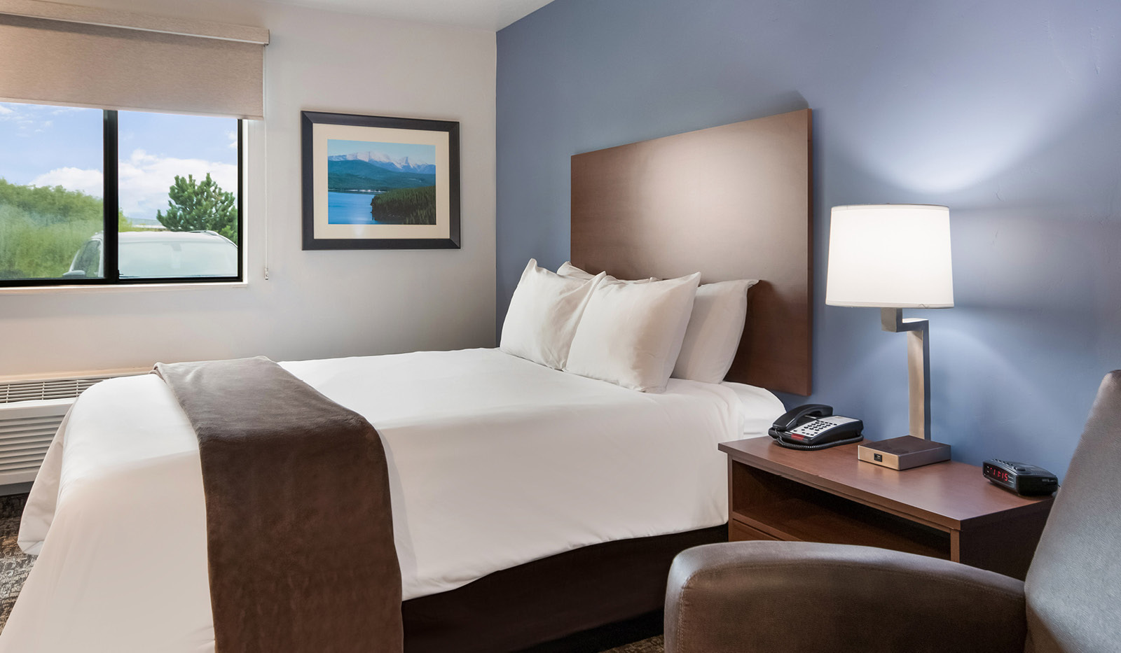 Interior room with single queen bed, bedside table and lamp, and brown recliner with a blue accent wall.