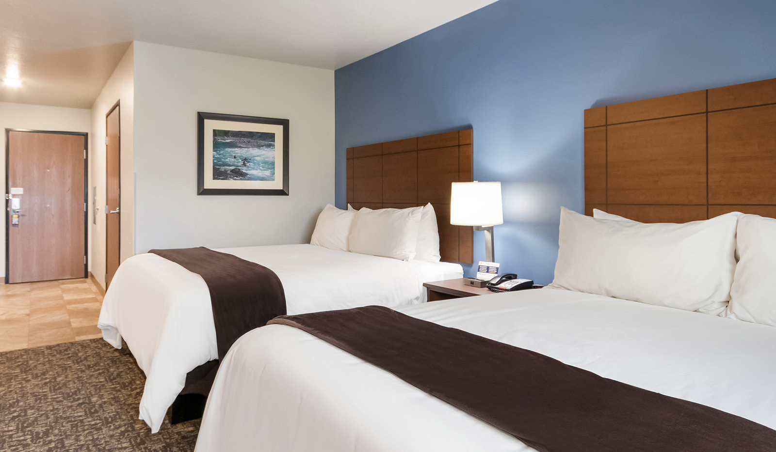 Interior hotel room facing door with two queen beds in front of a blue accent wall.