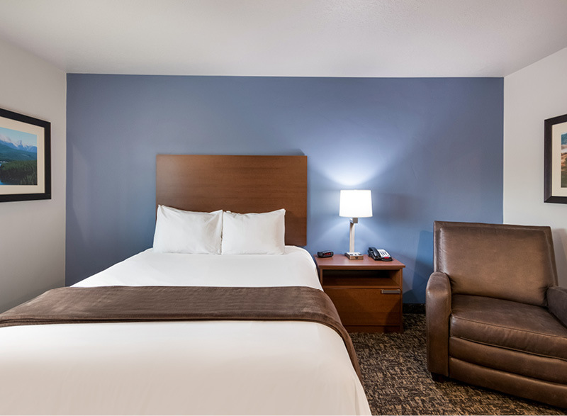 Interior room with single queen bed, bedside table and lamp, and brown recliner in front of blue accent wall.