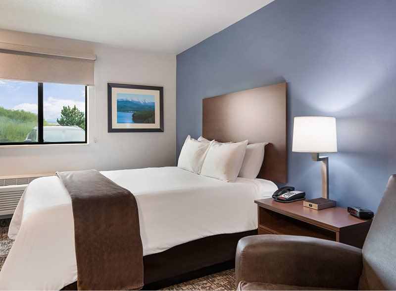 Interior room with single queen bed, bedside table and lamp, and brown recliner in front of blue accent wall.