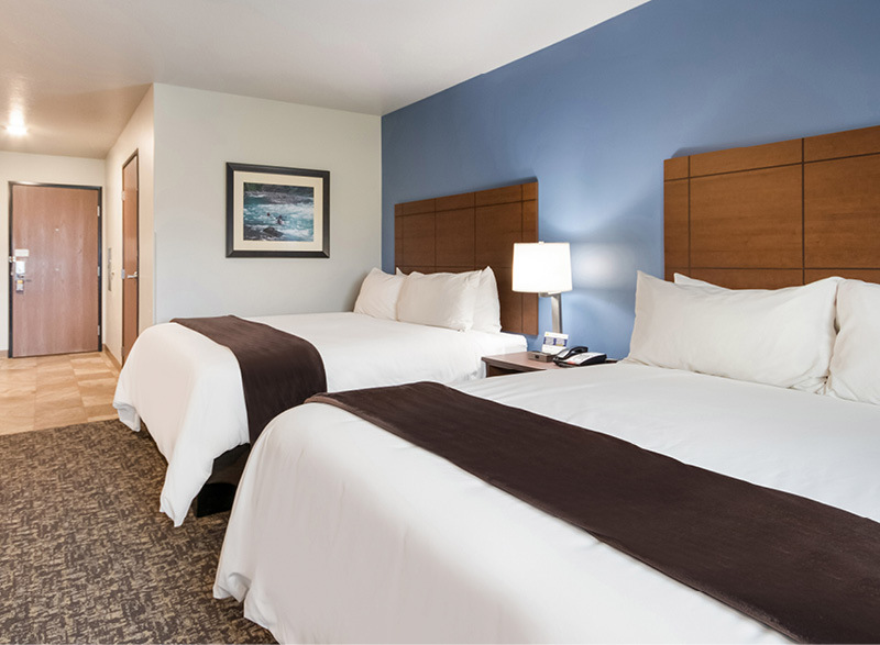 Interior hotel room facing the door with two queen beds in front of a blue accent wall.