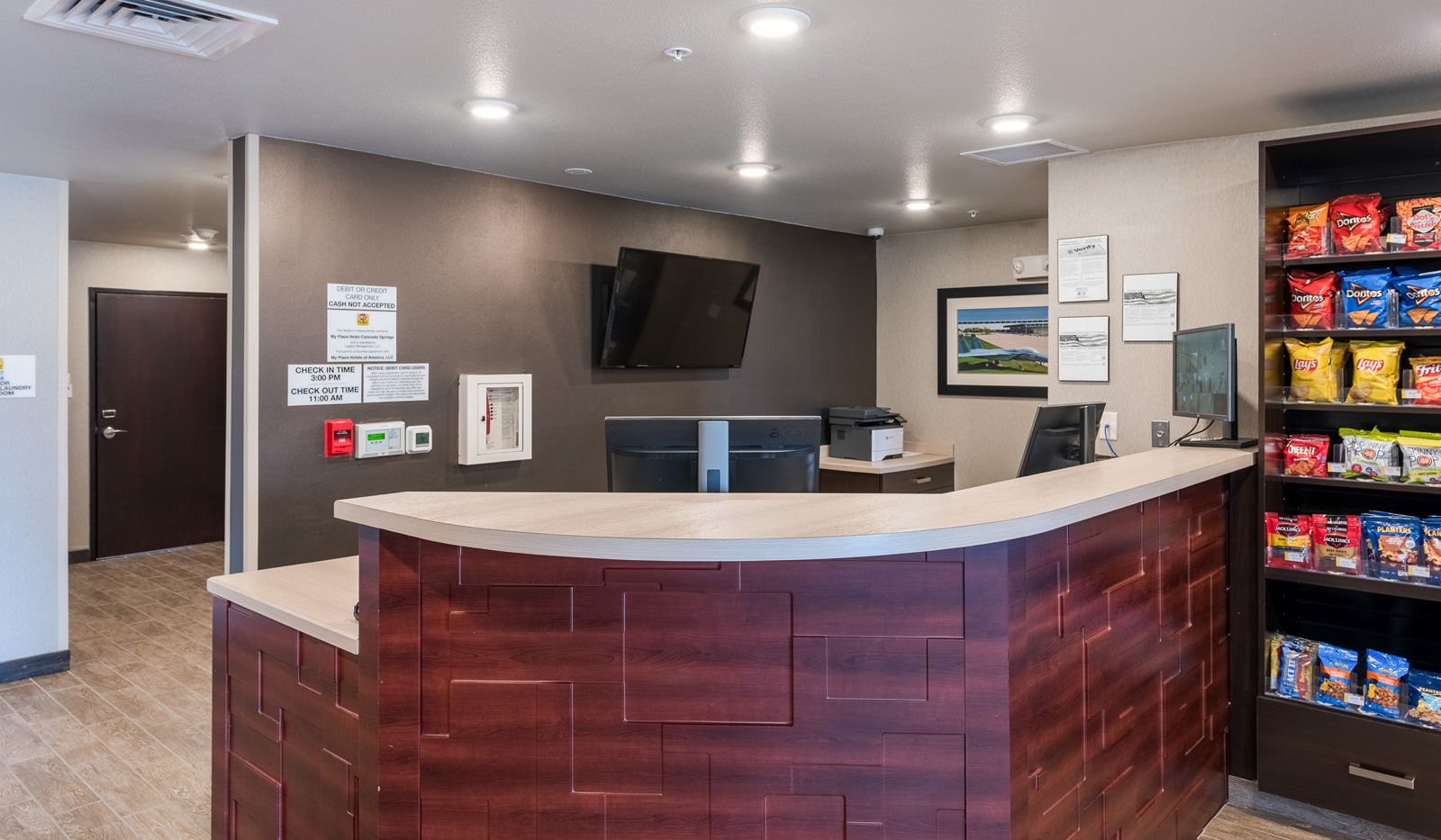 Interior lobby with brown front desk, mounted TV behind the desk, and racks of snacks to the right.