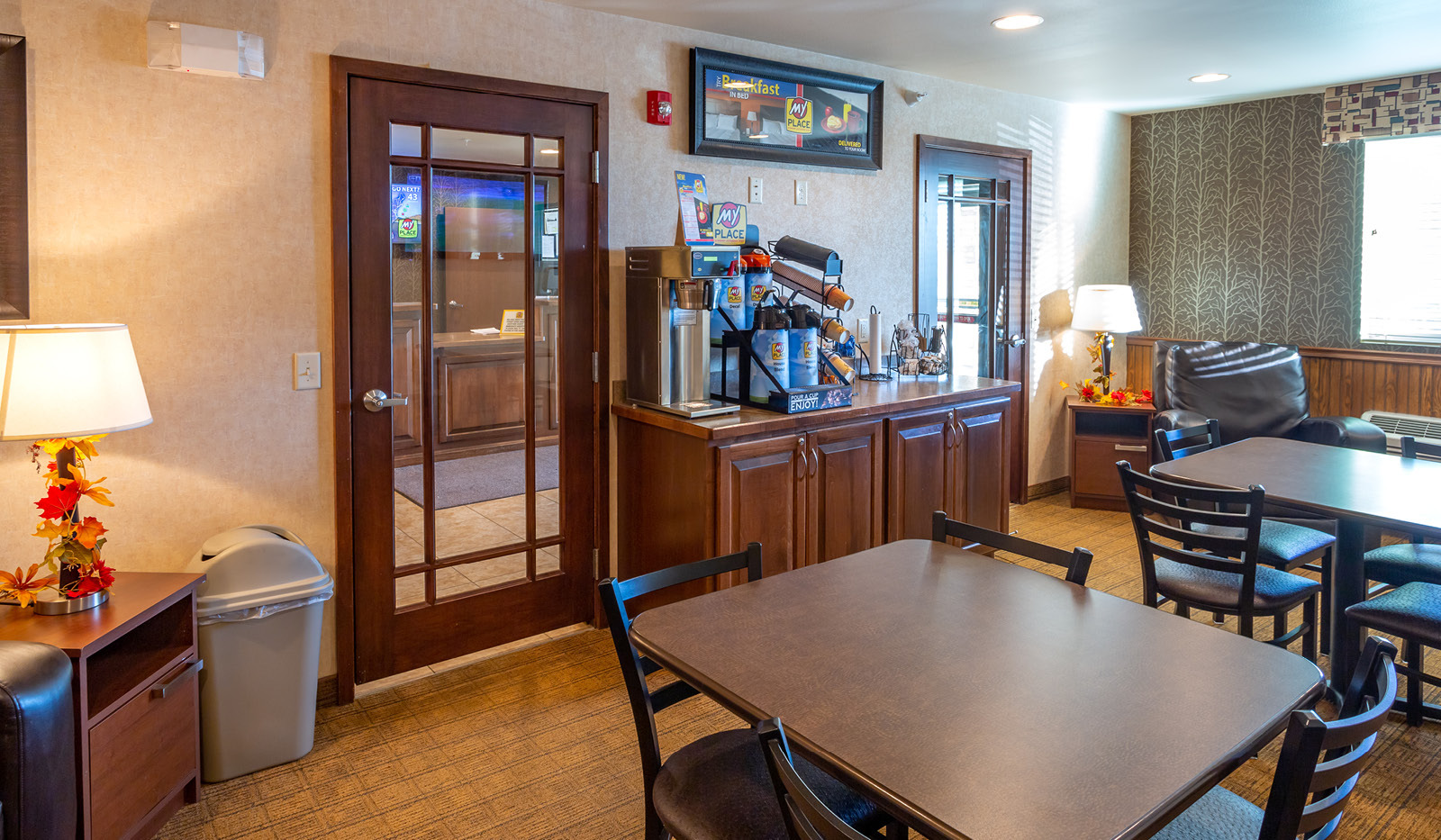 Interior lobby area with My Coffee station centered between two glass doors leading to front desk, and counter-height tables and chairs.