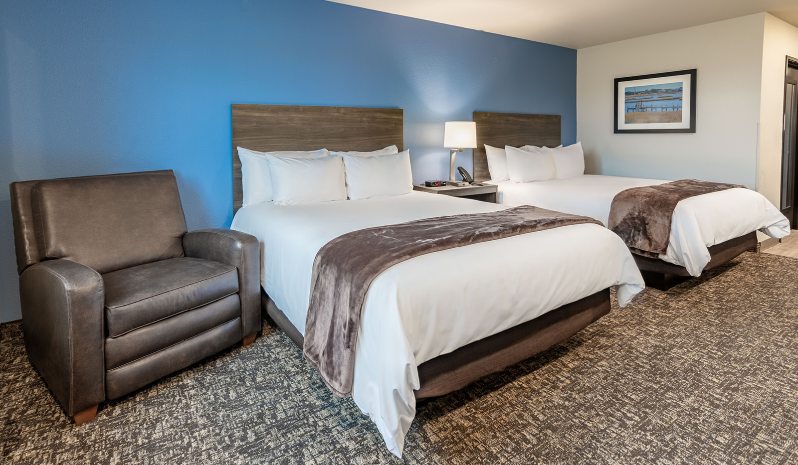 A hotel room featuring two beds and a recliner.