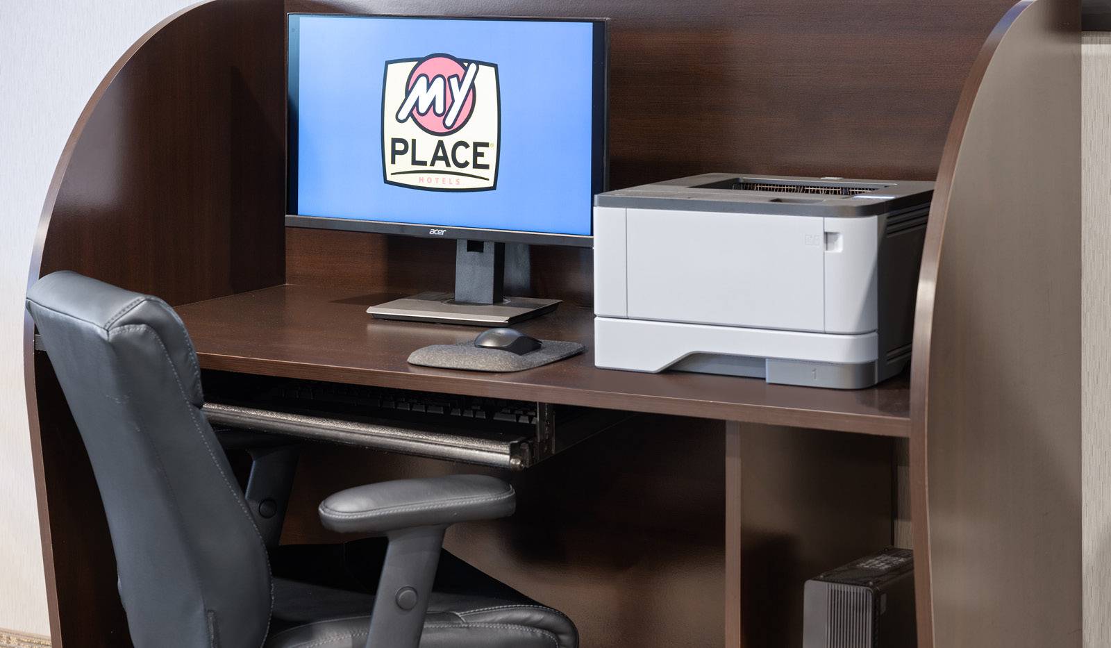 Lobby business center with computer showing My Place Hotels logo, a printer and a desk chair waiting to be used.