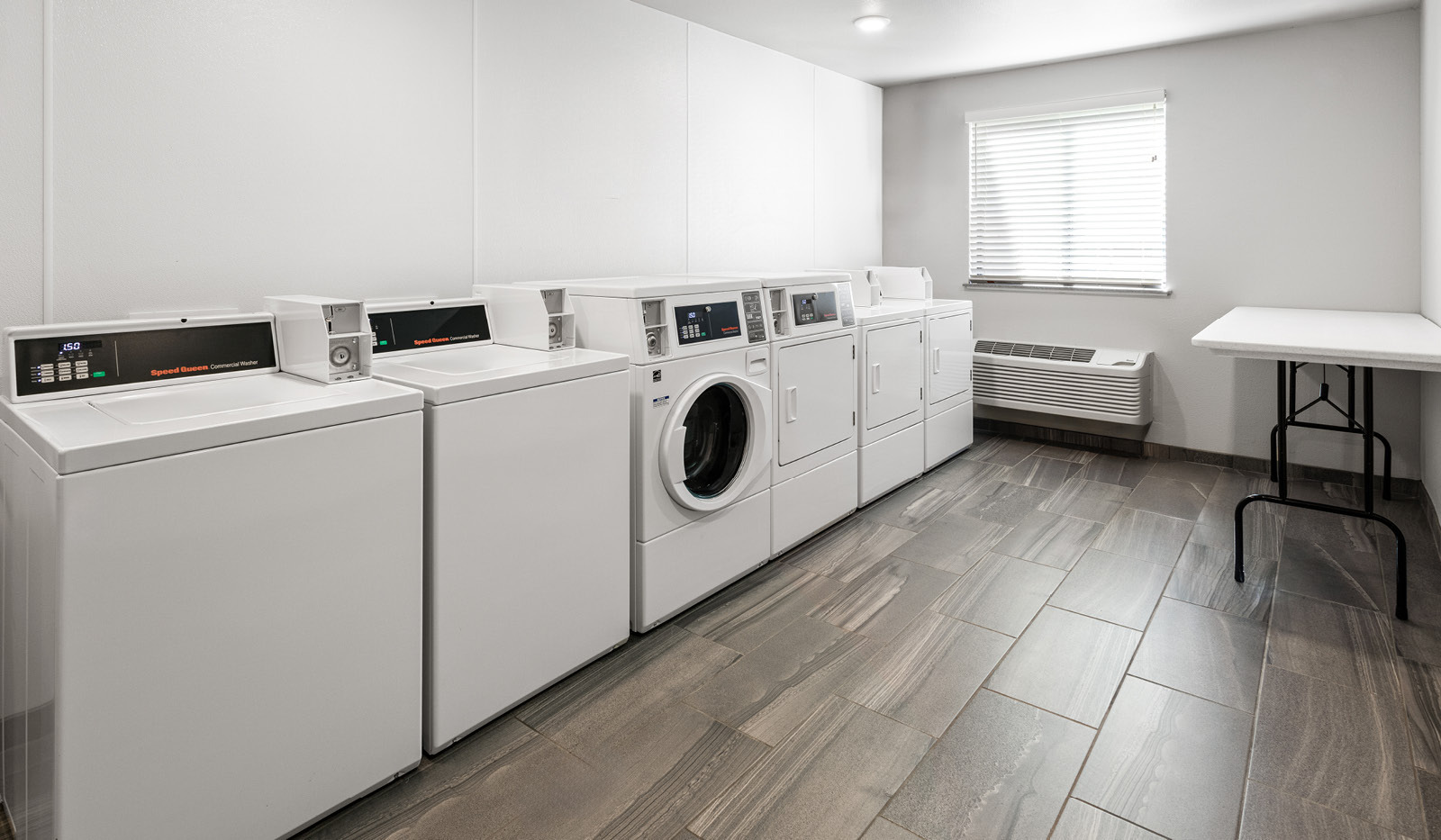 Clean laundry facility with multiple washing machines, dryers and a table for folding clothes.