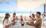 Group of people eating on an outdoor bench at the beach.