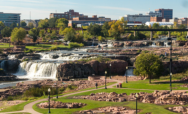 A series of small waterfalls surrounded by landscaped park and city buildings in the background: Falls Park, Sioux Falls, South Dakota