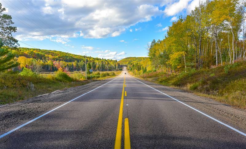 A highway bisects a green forest under a partly cloudy blue sky.