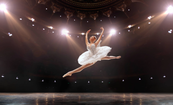 A woman in a white tutu leaps across a stage lit with lights.