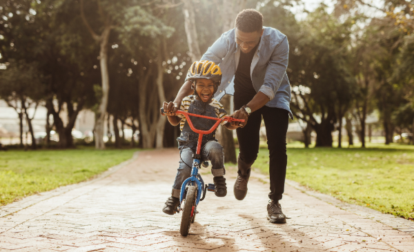 A dad helps his young son learn to ride a bike in a park.