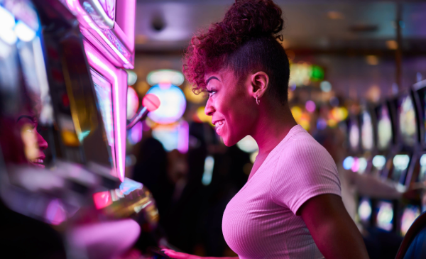 A side profile of a woman sitting at a casino machine, her face reflecting a purple hue from the game.