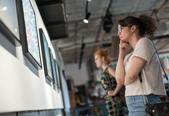Low angle of two women looking at framed art on a wall.