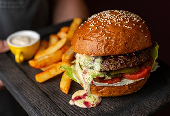 A burger dripping sauce, fries, and a small latte, all on a black wooden block.