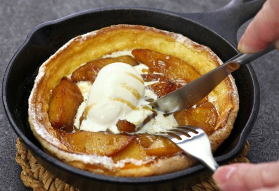 Utensils cutting a Dutch pancake inside a cast iron pan.