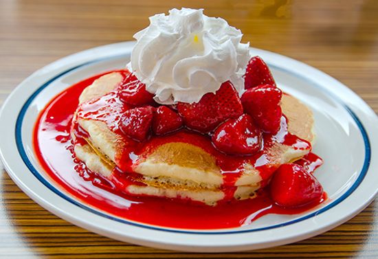 Classic looking pancakes with strawberry sauce and whipped cream.
