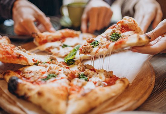 Close view of multiple hands grabbing pizza slices.