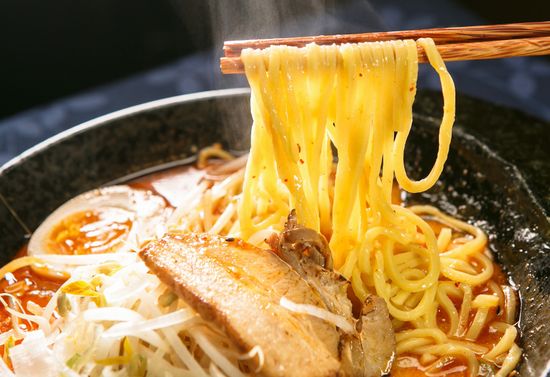 A pair of chopsticks holding up some ramen noodles above a bowl of ramen.