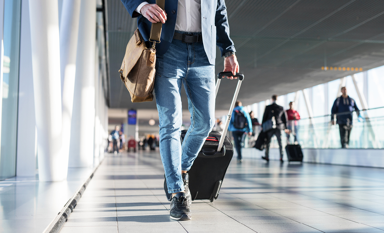 Multiple people pulling a suitcase walking down a hallway with floor to ceiling windows.