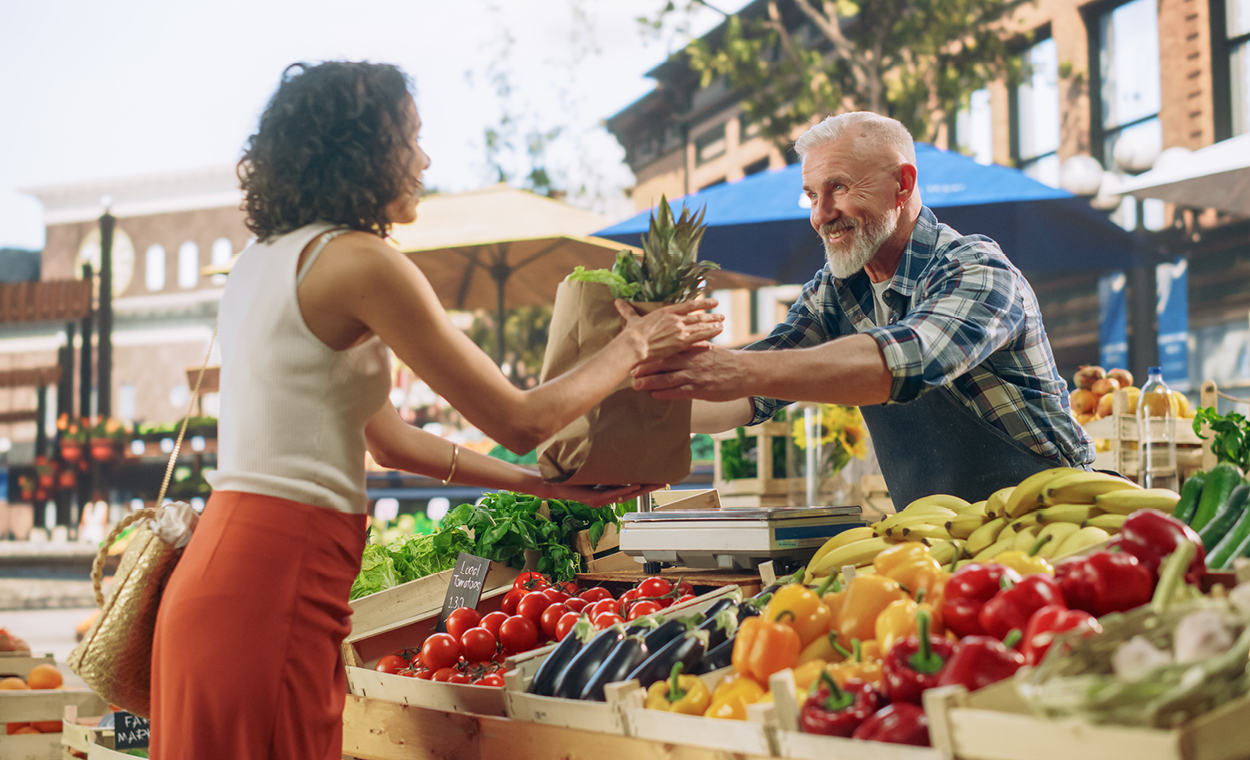 Women buying fruit and vegetables from a stand at a farmers market.